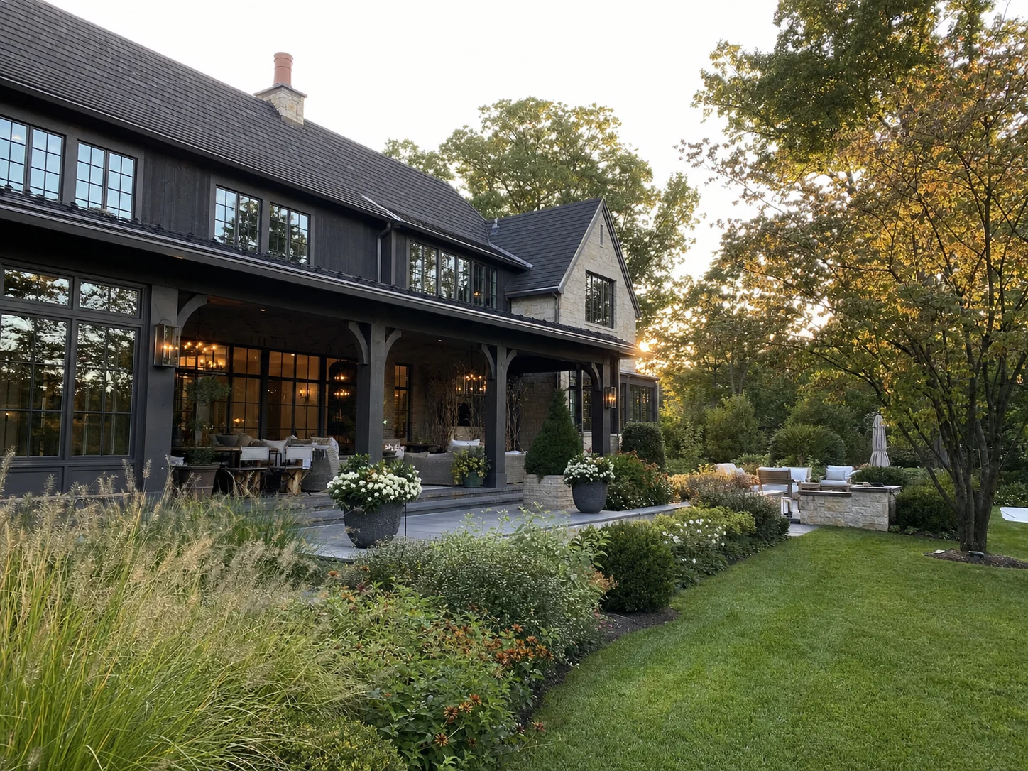 High-end stone and dark-wood home opening onto a mature landscaped backyard in warm late-afternoon light